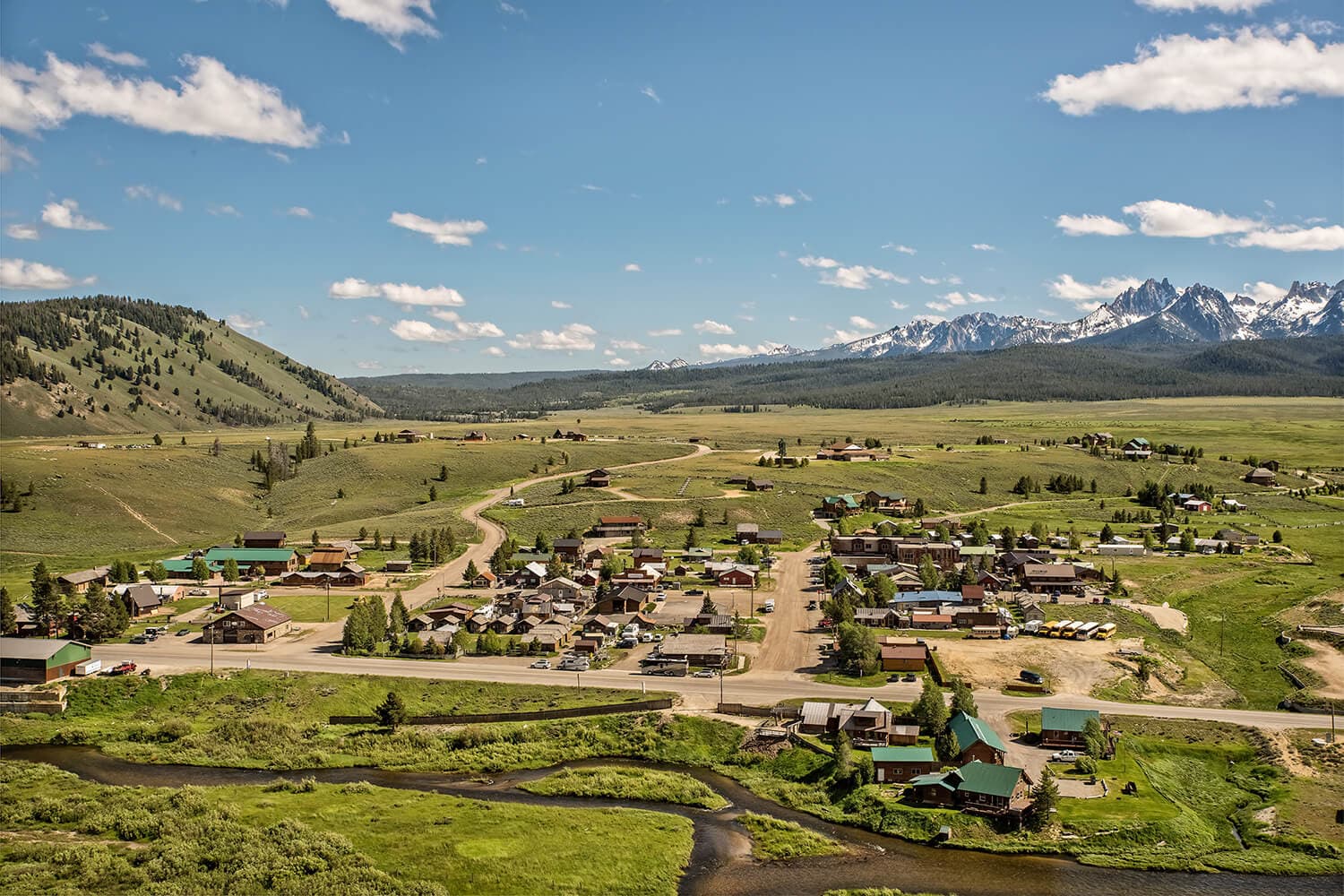 Aerial view of a small town surrounded by green fields and mountains under a blue sky.