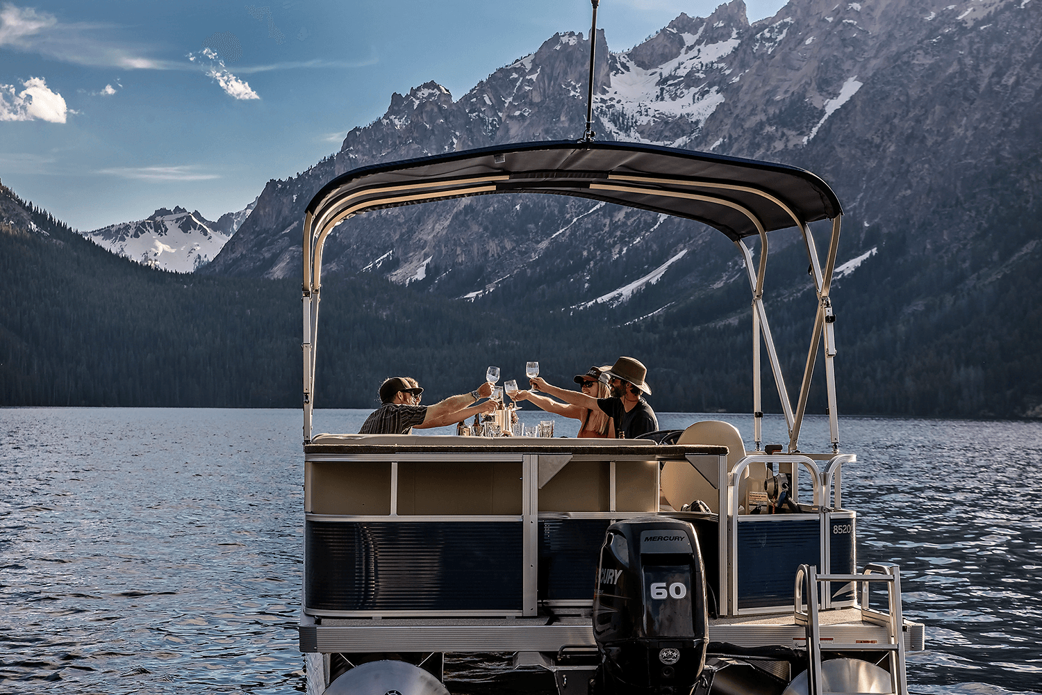 Two people on a boat toast with glasses against a scenic mountain backdrop.