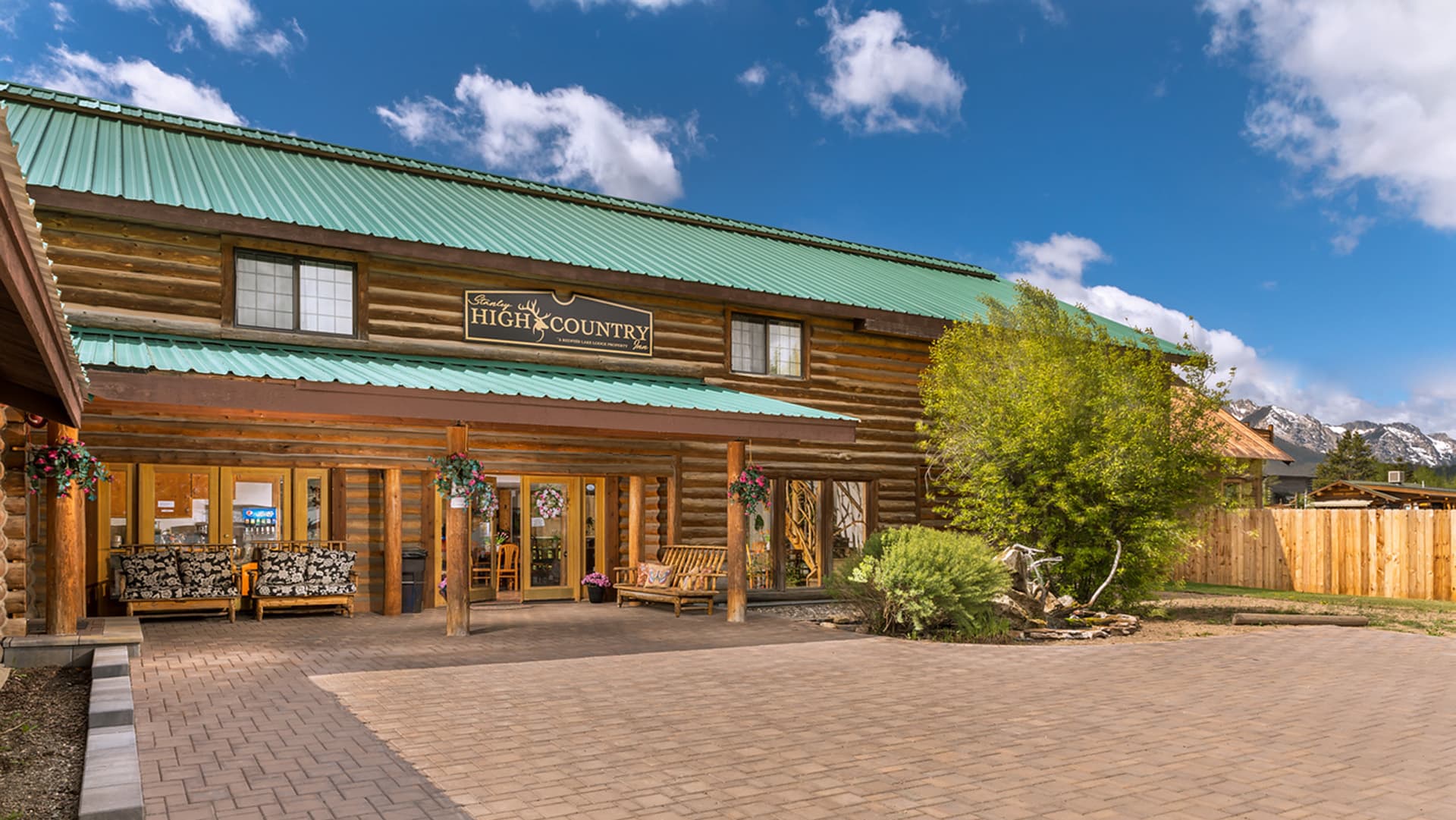 A log cabin-style building with a green metal roof and "High Country" sign, surrounded by landscaping and open skies.