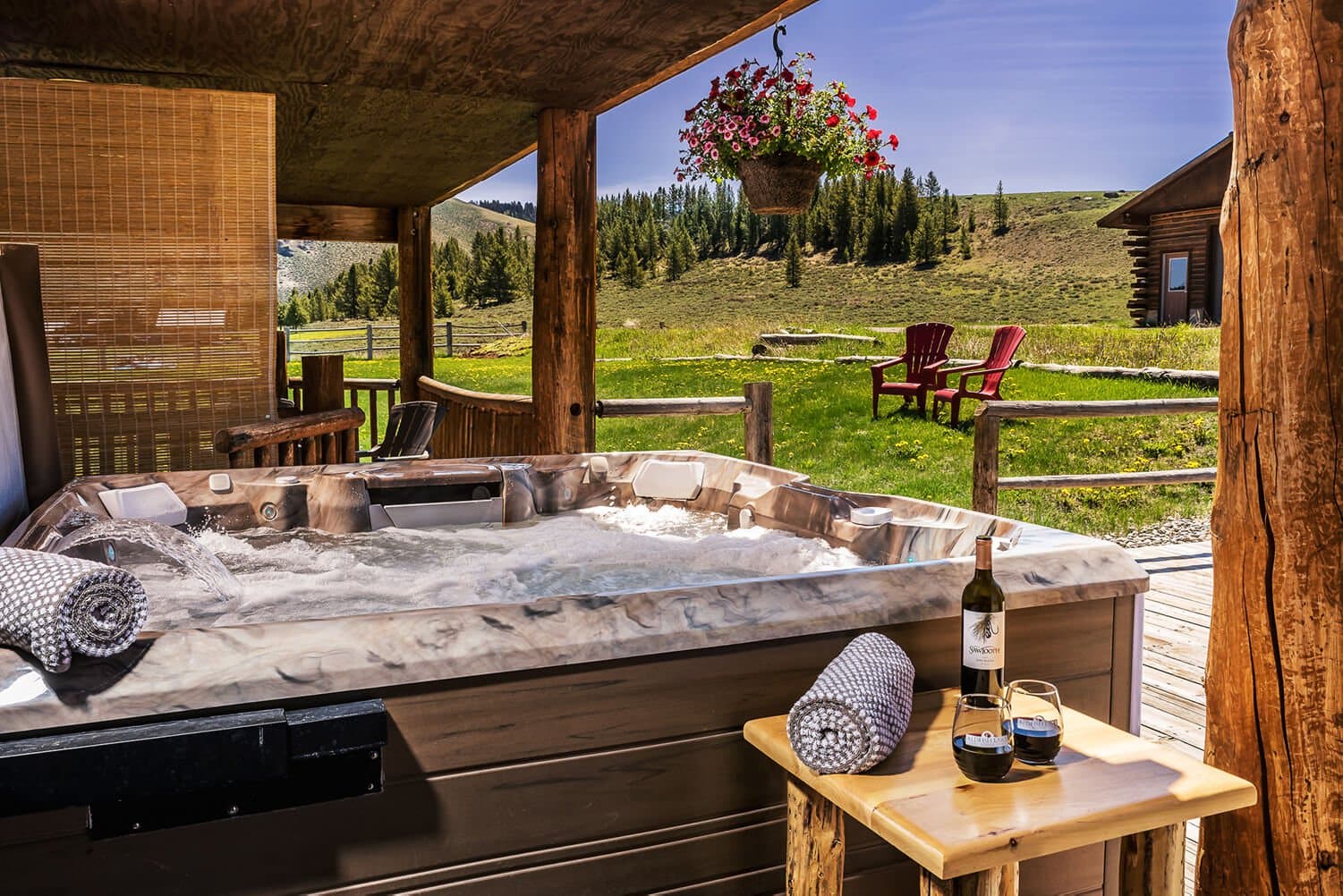 A hot tub on a wooden deck with a scenic view, accompanied by a bottle of wine and two glasses.